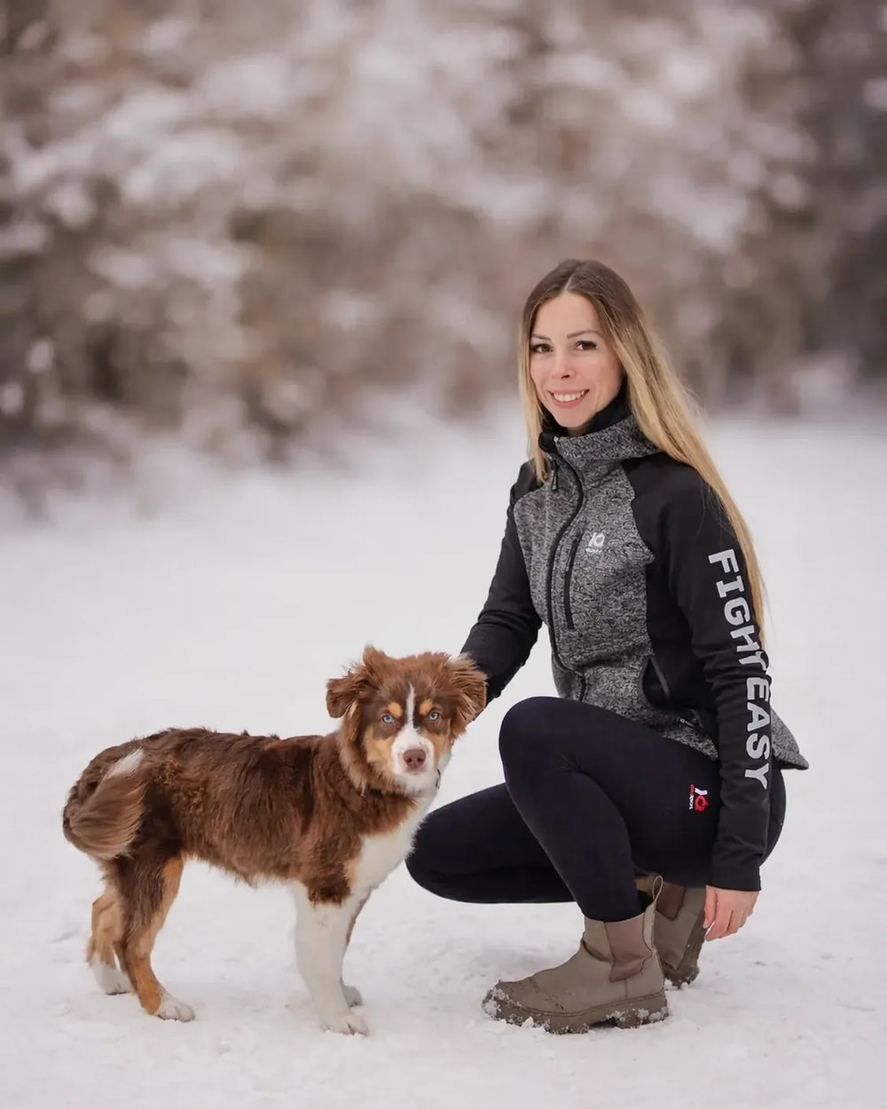 Woman in a grey and black IQ zip hoodie with an Aussie in the snow
