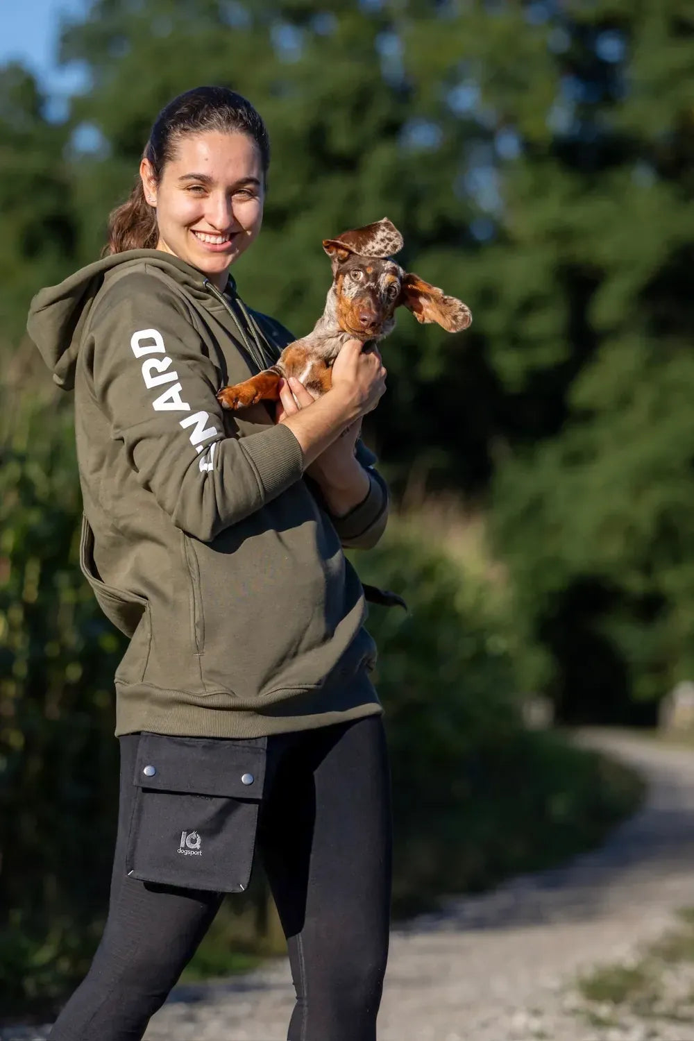 Woman in an olive IQ hoodie with the optional modular treat pocket and a dachshund