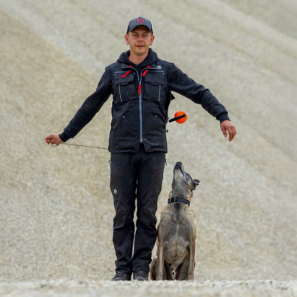 Handler in an IQ dog sport vest, ball dropping from the chest pocket