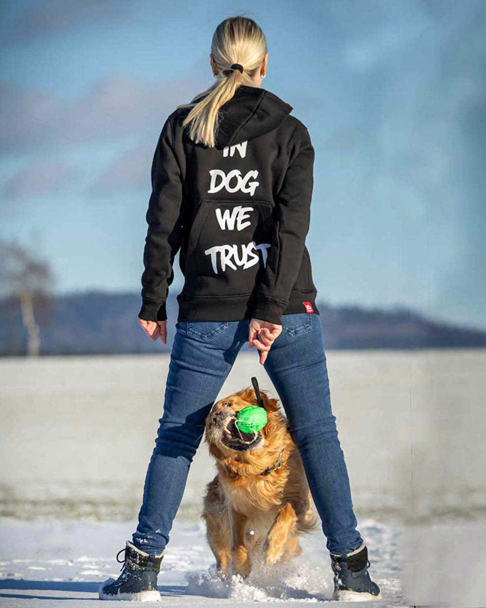 Rear view of an IQ training hoodie with a print, with a dog at heel in the snow